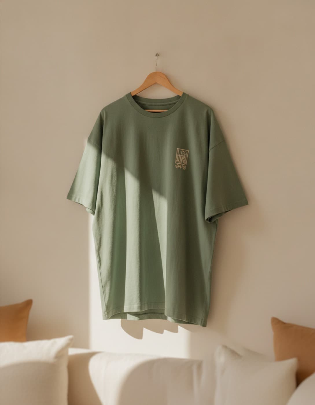 Camiseta oversize verde jade colgada de una percha, con un estampado pequeño al pecho