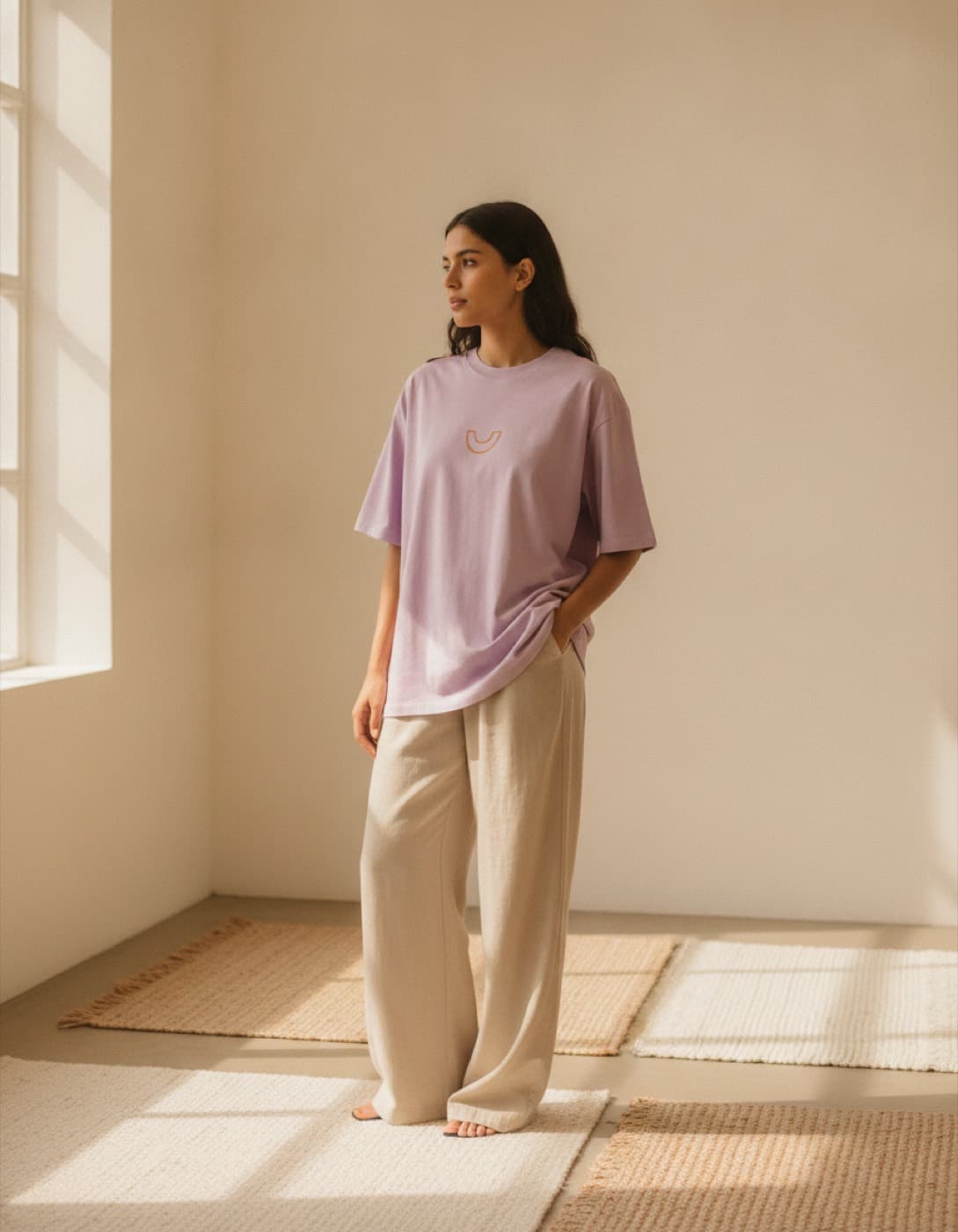 Persona con una camiseta oversize lila y pantalón ancho, de pie en una sala luminosa